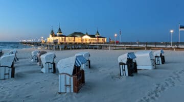 Hooded beach chairs and illuminated pier on sand coast