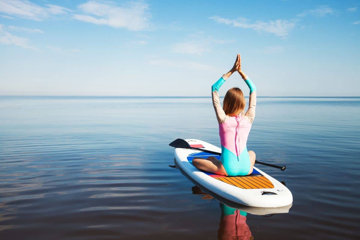 Eine Frau macht Yoga auf einem SUP - eines der Dinge auf ihrer Sommer Bucket List